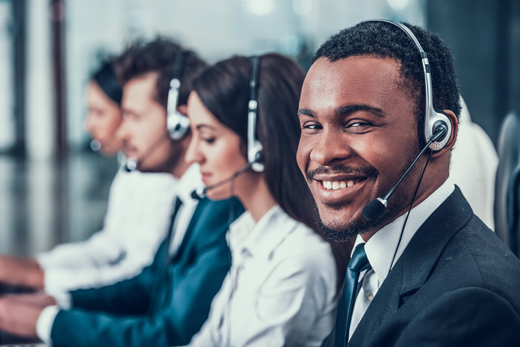 A variety of people sitting in a row at a call center, providing support on headsets.