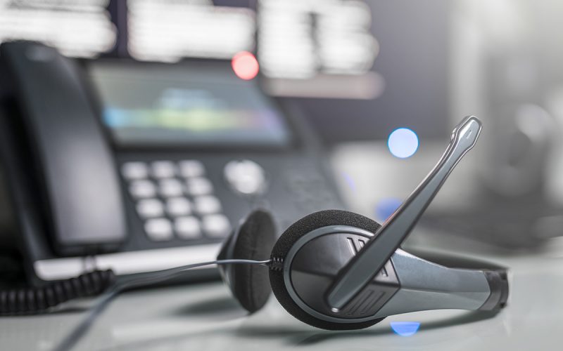 An image of a VoIP headset with a standard business landline behind it, less in focus.