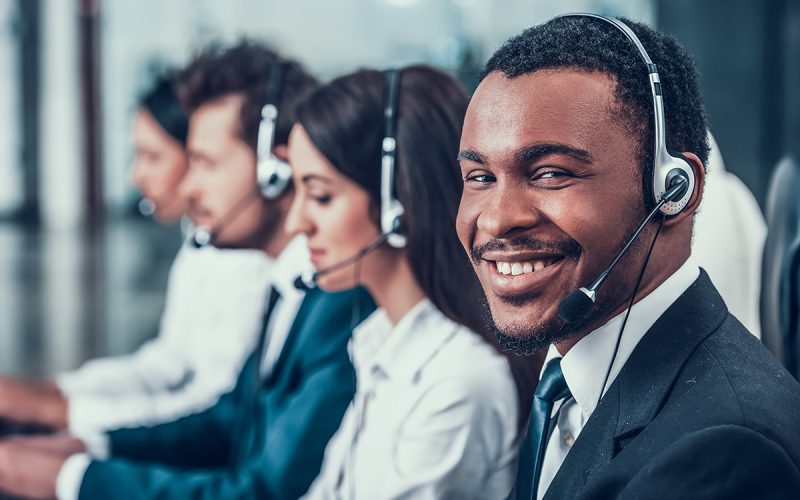 A variety of people sitting in a row at a call center, providing support on headsets.